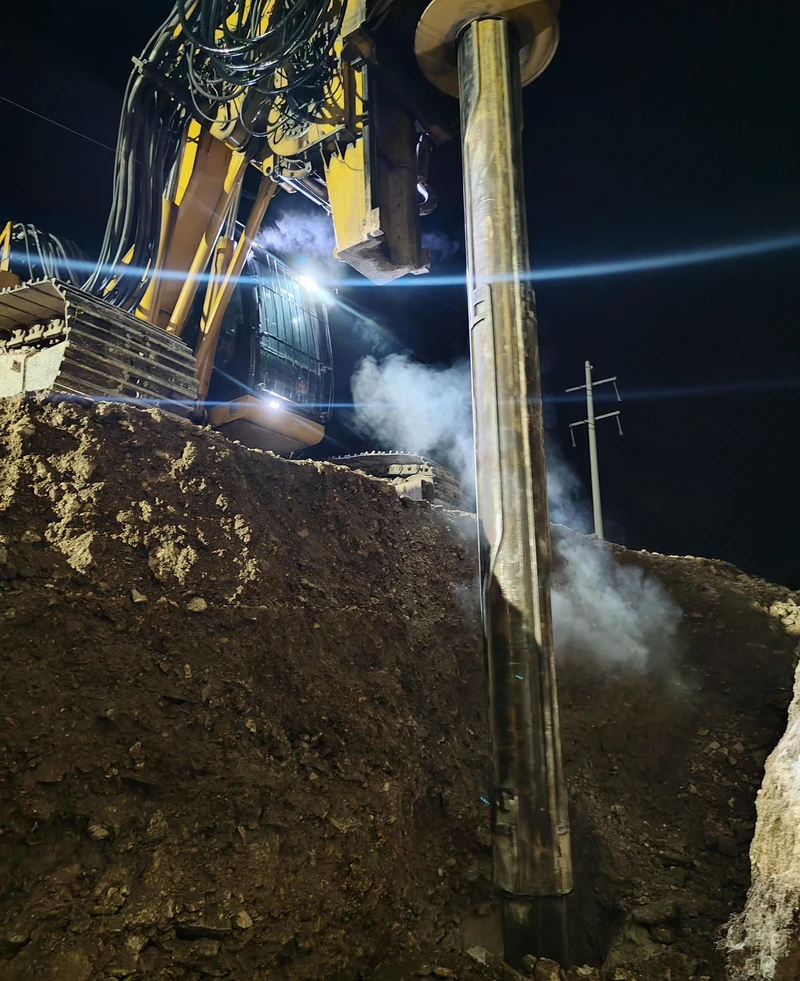Perforadora trabajando de noche dentro de la excavación, con el bote corona descendiendo al barreno